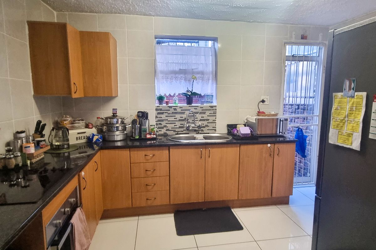 A functional kitchen featuring wooden cabinetry, granite countertops, a built-in oven, and tiled finishes with direct access to an exterior area.