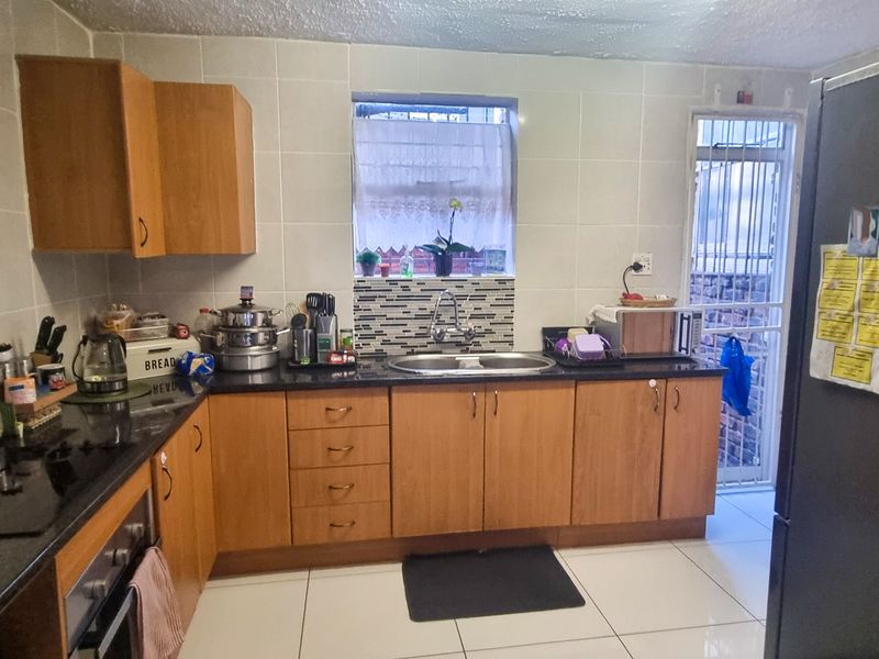 A functional kitchen featuring wooden cabinetry, granite countertops, a built-in oven, and tiled finishes with direct access to an exterior area.