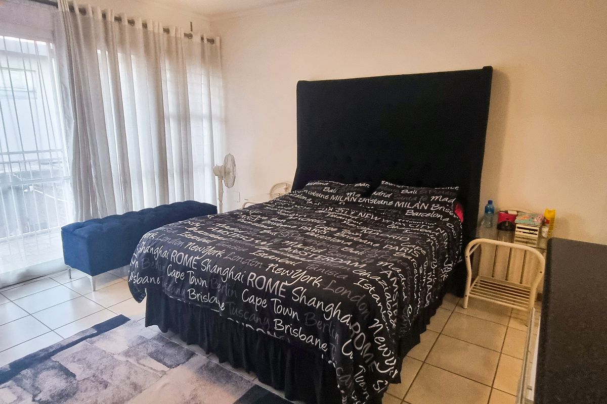 A bedroom featuring tiled flooring and a sliding glass door with security gate, providing access to an outdoor area.