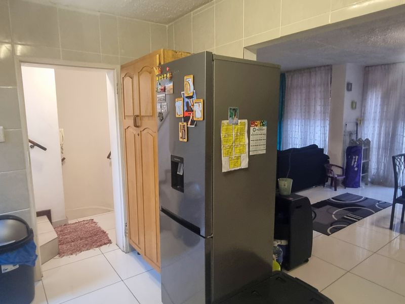 Open plan living area featuring tiled flooring and wall tiles, connecting the kitchen space to the dining and living zones.