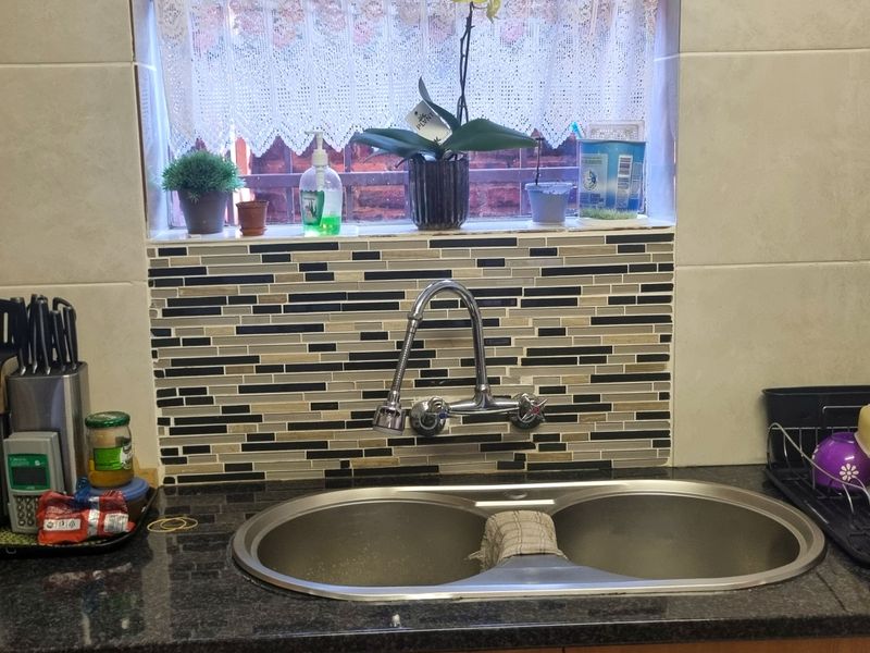 A functional kitchen sink area featuring a double bowl stainless steel sink, gooseneck faucet, granite countertops, and a decorative mosaic tile splashback.