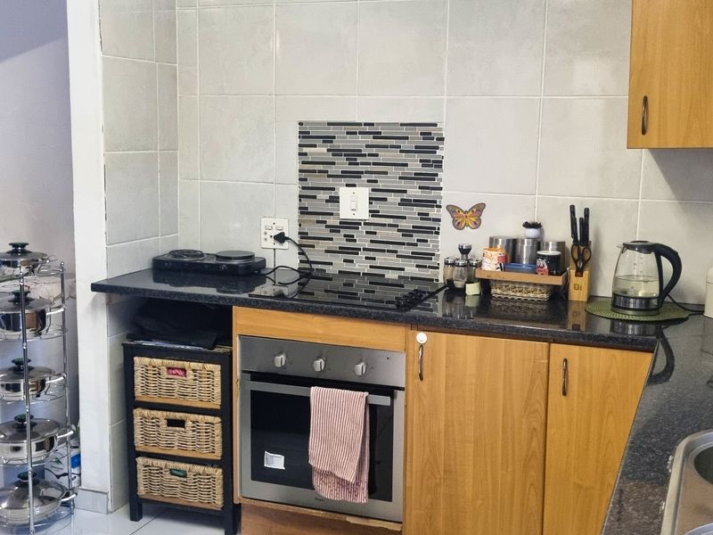 A functional kitchen featuring laminate cabinetry, granite countertops, a built-in oven, and a tiled backsplash with a decorative mosaic accent.