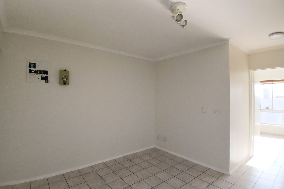 An empty, neutrally painted living area featuring tiled flooring, a ceiling spotlight, and an integrated intercom system.