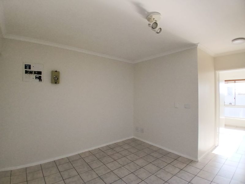 An empty, neutrally painted living area featuring tiled flooring, a ceiling spotlight, and an integrated intercom system.