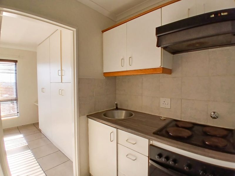 Compact kitchen featuring built-in cabinetry, electric hob, oven, extractor fan, and tiled splashback, leading into an adjacent hallway with additional storage.
