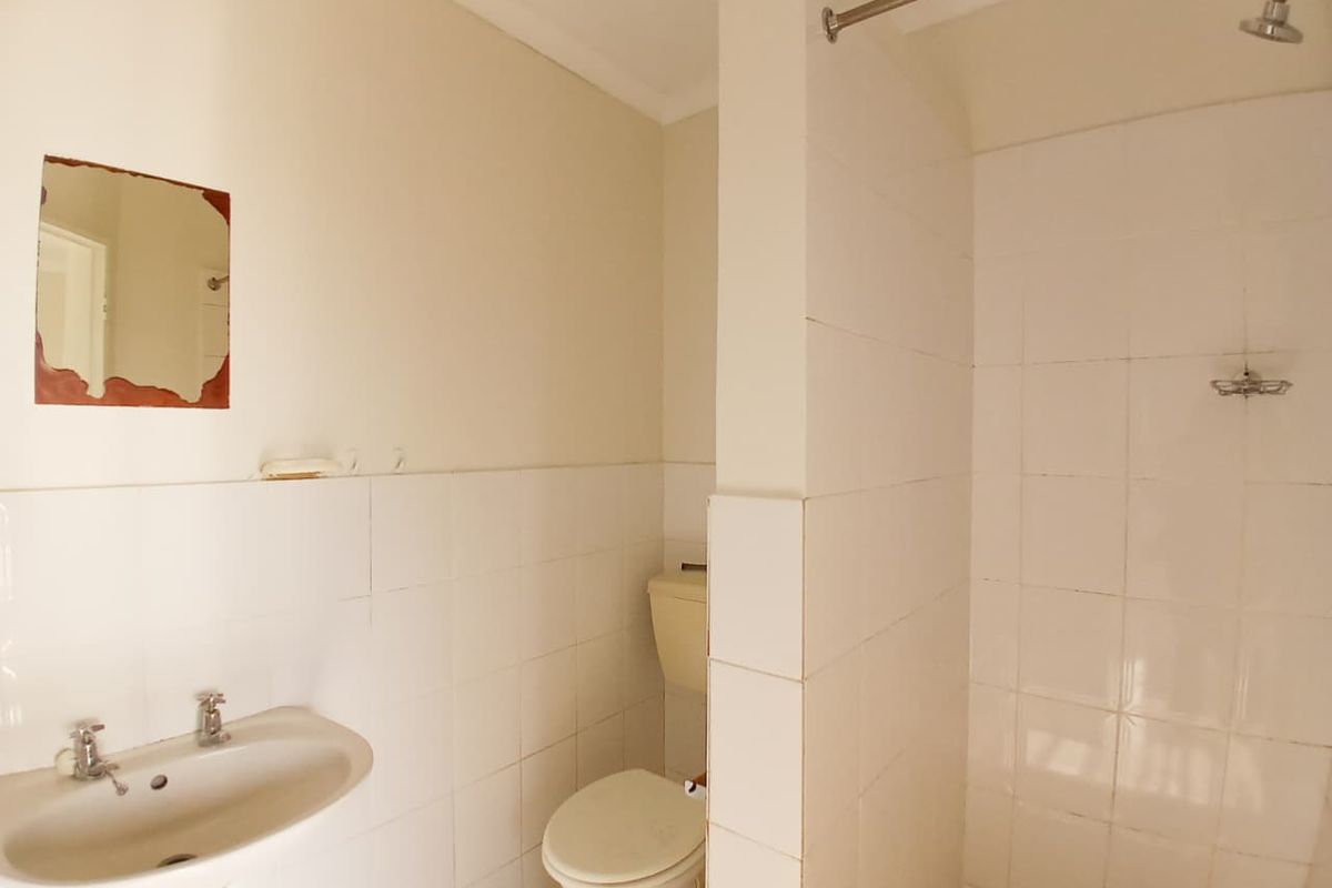 A functional bathroom featuring a wall-mounted basin, toilet, and a tiled shower area with a partition wall.