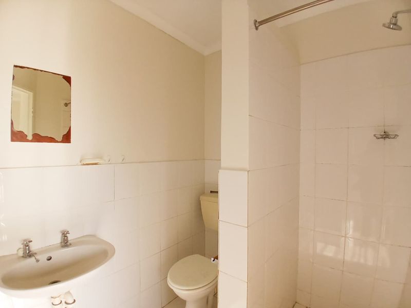 A functional bathroom featuring a wall-mounted basin, toilet, and a tiled shower area with a partition wall.