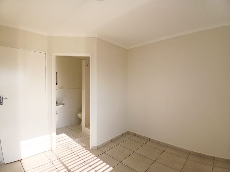 A bright, empty bedroom featuring neutral tiled flooring and direct access to an en-suite bathroom.