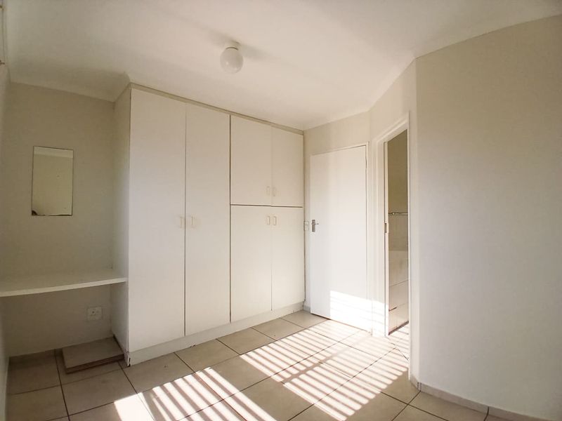 A vacant bedroom featuring built-in cupboards, tiled flooring, and a built-in vanity shelf, with direct access to an adjacent bathroom.