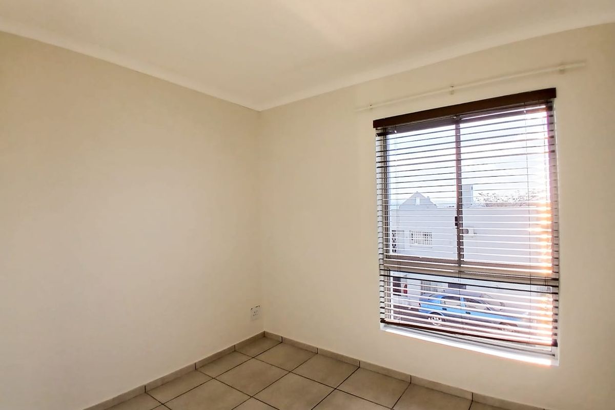 A bright, empty bedroom featuring neutral tiled flooring and fitted venetian blinds, offering a clean canvas for personalization.