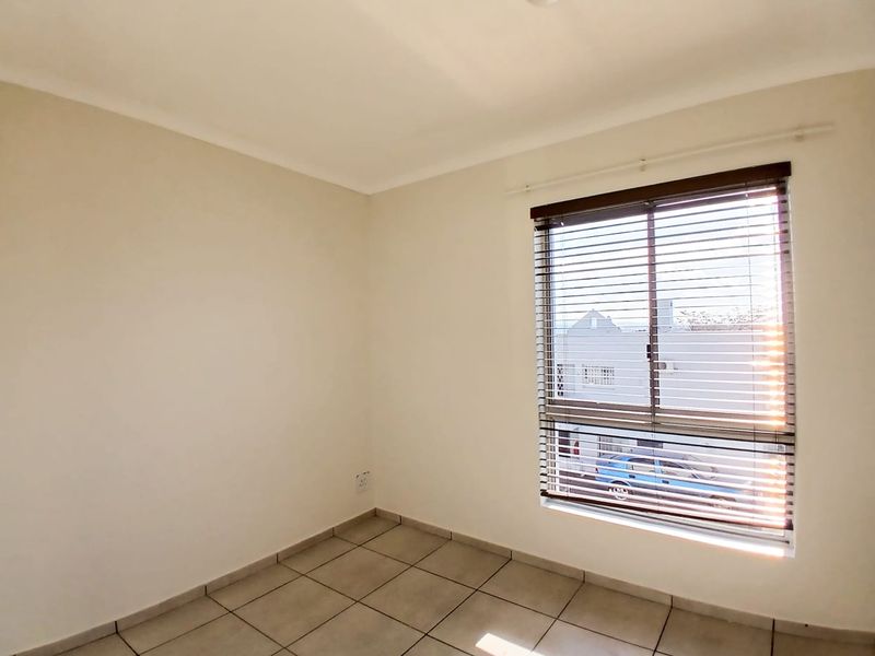 A bright, empty bedroom featuring neutral tiled flooring and fitted venetian blinds, offering a clean canvas for personalization.