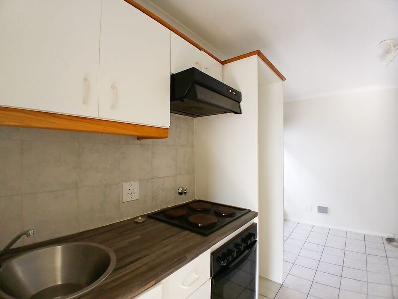 A functional kitchen featuring built-in cabinetry, a laminate countertop, a stainless steel sink, and an integrated electric oven and hob with an extractor fan.