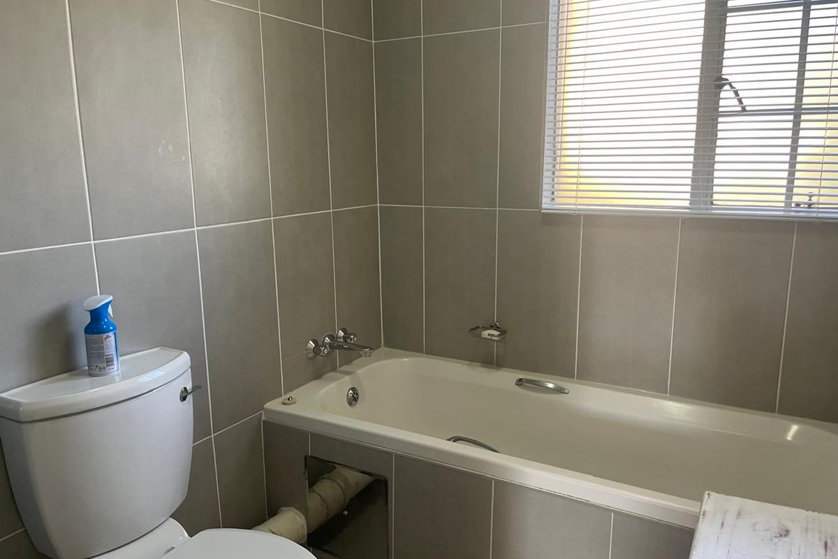 A functional bathroom featuring tiled walls, a built-in bathtub, and a toilet, with a window providing natural light.