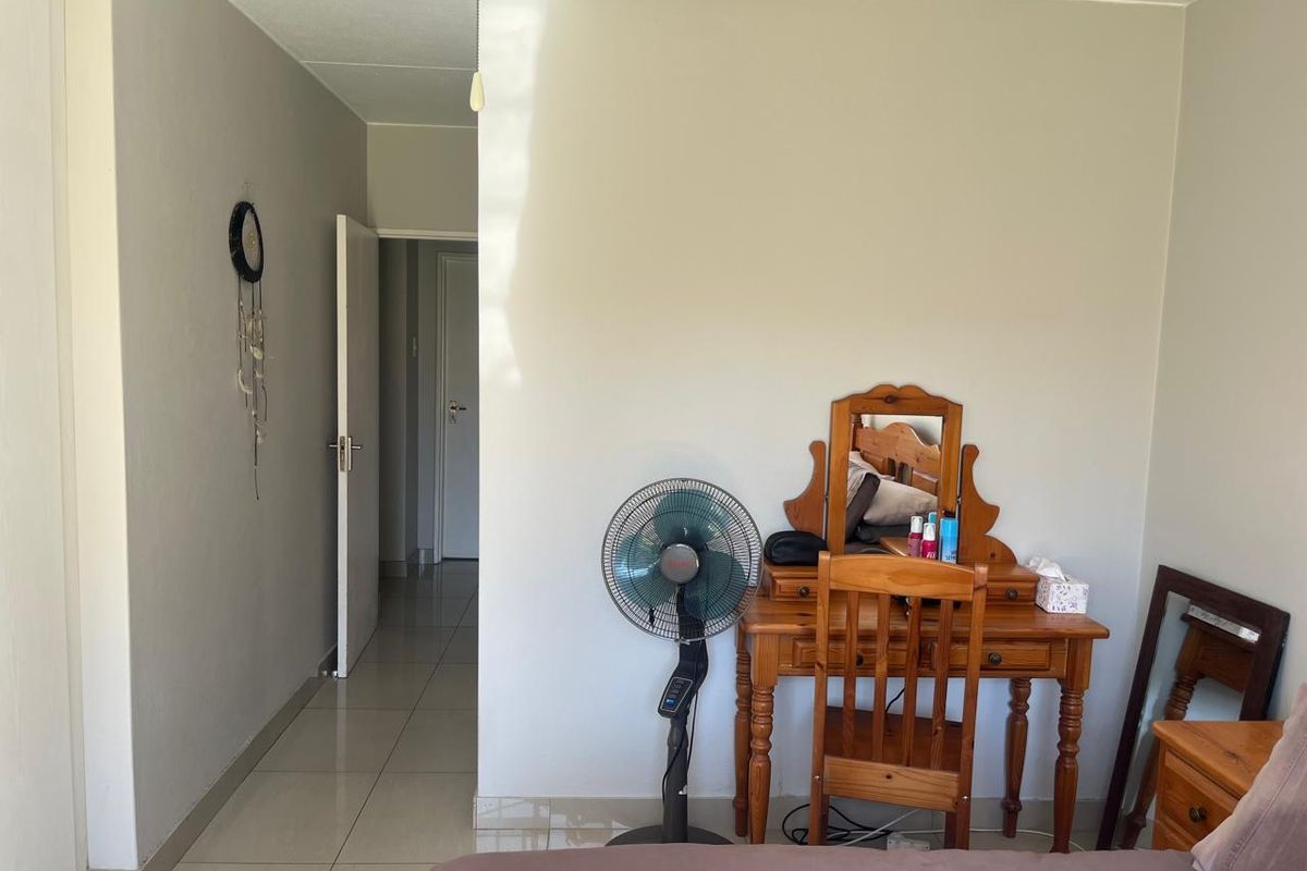 A bedroom interior featuring tiled flooring and access to an adjoining hallway.