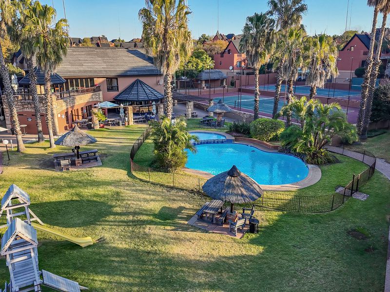 Aerial view of a well-maintained apartment complex communal area featuring a swimming pool, tennis court, landscaped gardens, and outdoor entertainment facilities.