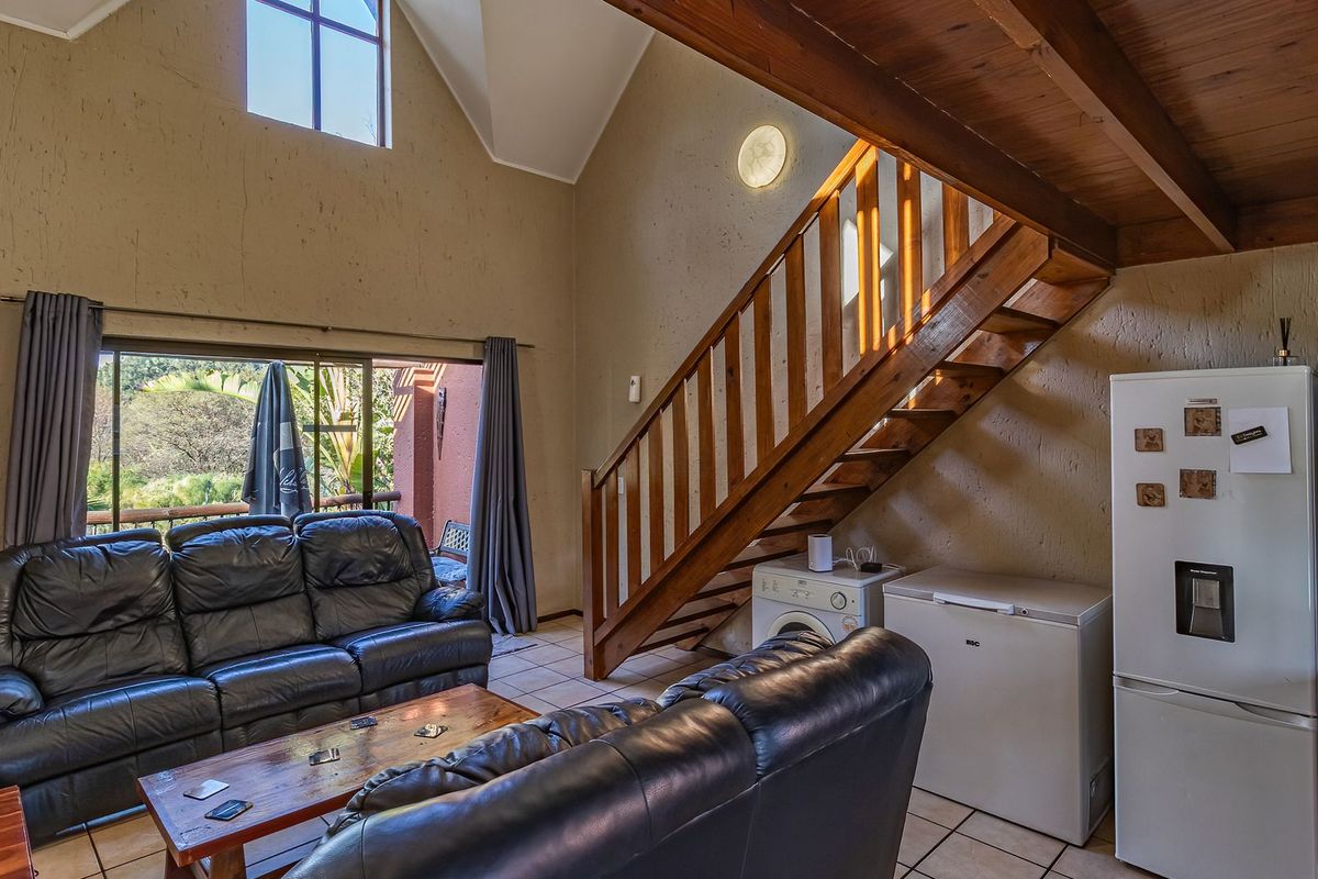 Spacious living area featuring a vaulted ceiling with exposed timber beams, a wooden staircase, tiled flooring, and direct access to an outdoor balcony.