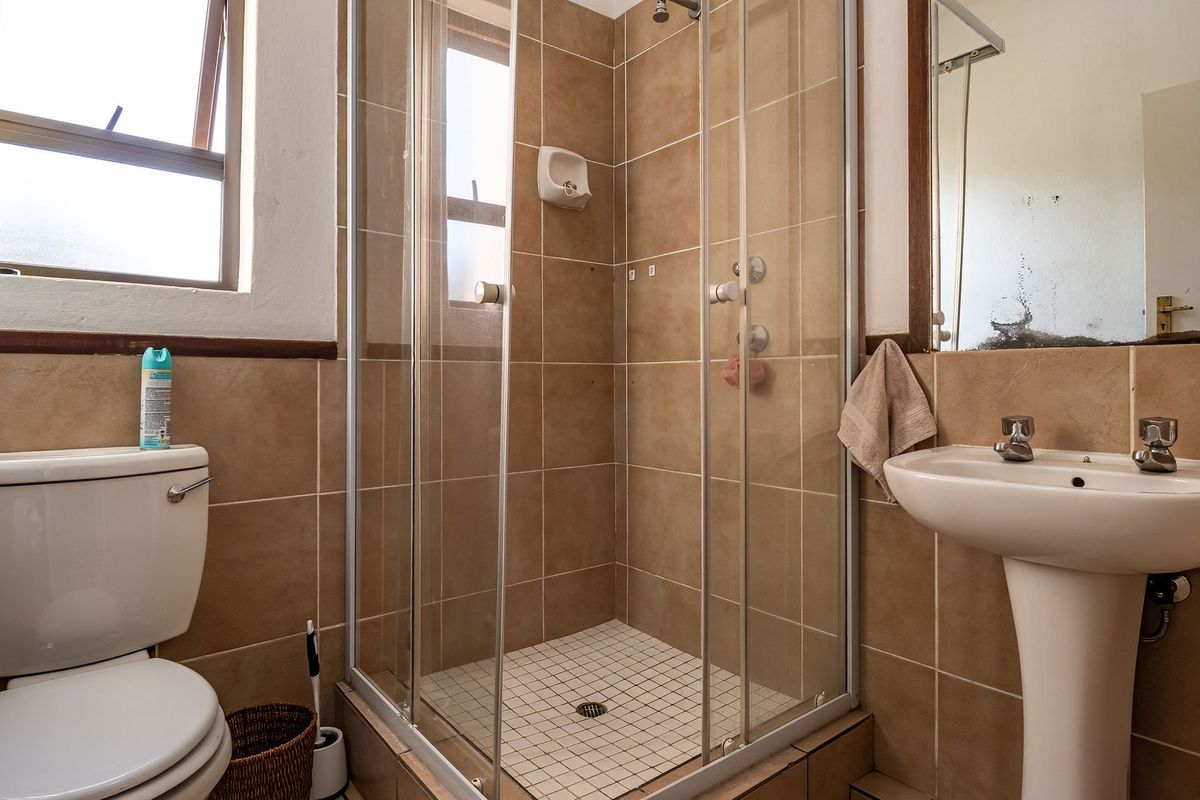 A functional bathroom featuring a tiled shower enclosure, pedestal basin, and toilet, with neutral wall tiling throughout.