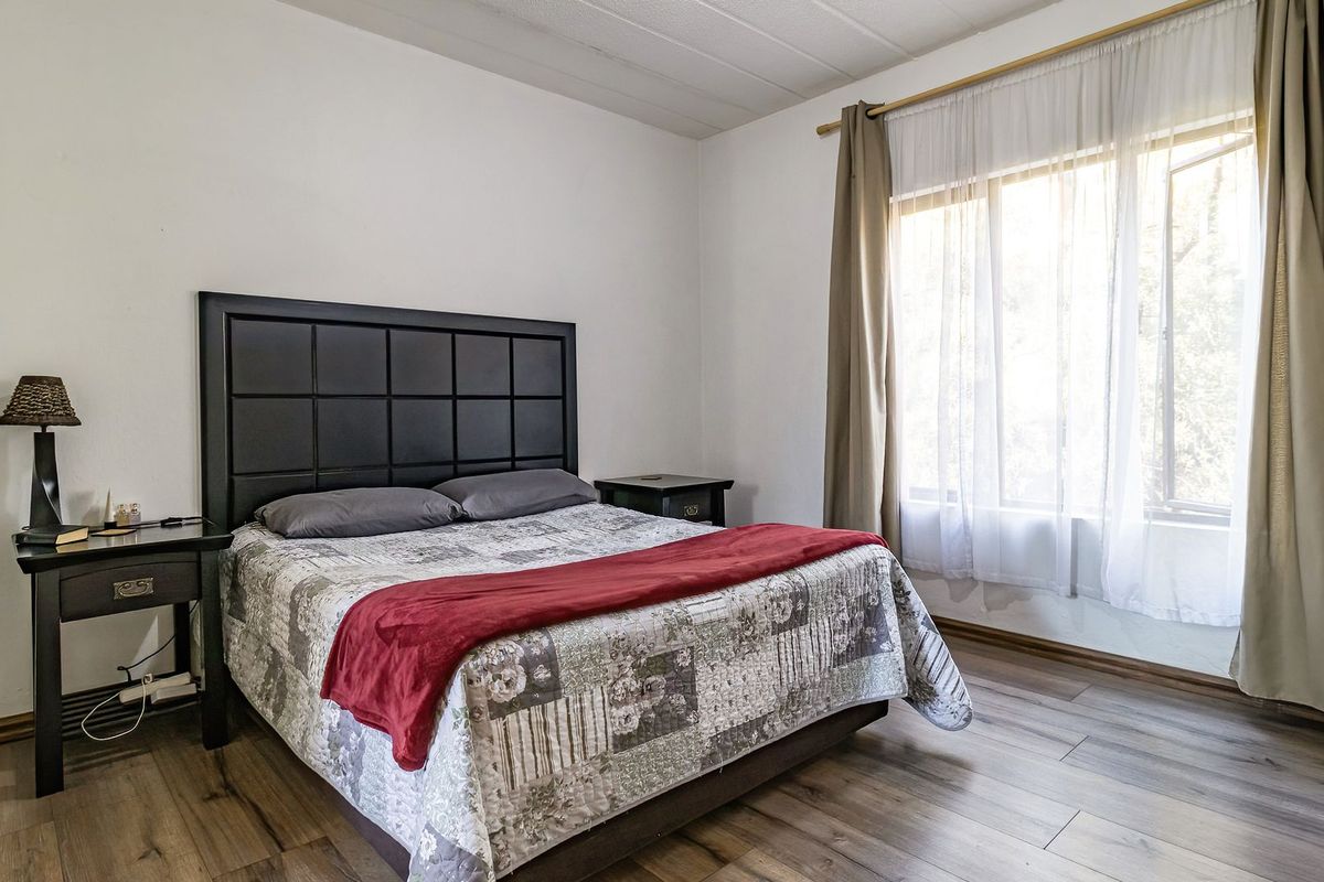 A bedroom featuring laminate flooring and natural light from a large window with curtain fixtures.