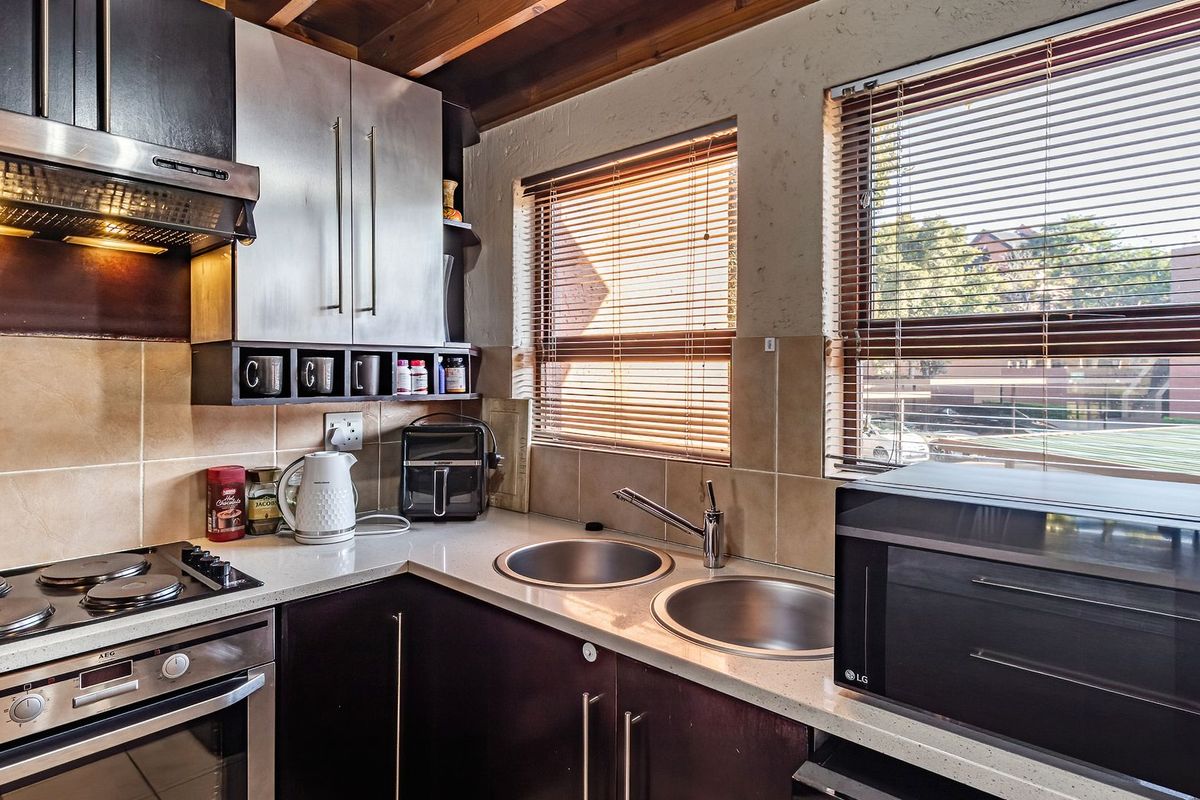 A functional kitchen featuring dark cabinetry, stone countertops, a double sink, and built-in appliances including an oven and extractor fan.