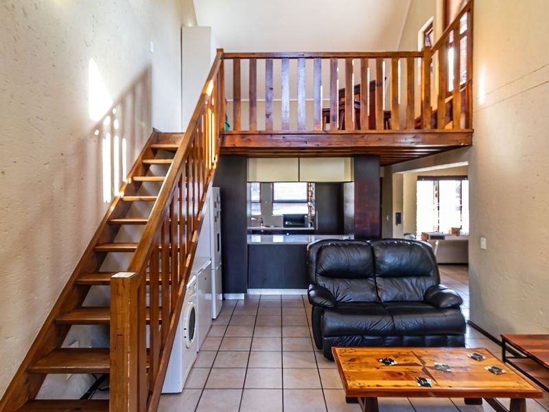 Open plan living area featuring a wooden staircase leading to a mezzanine level, with an integrated kitchen and tiled flooring throughout.