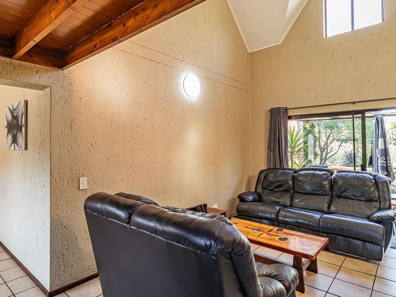 Spacious living room featuring a vaulted ceiling with exposed timber beams, tiled flooring, and a sliding glass door leading to an outdoor patio area.