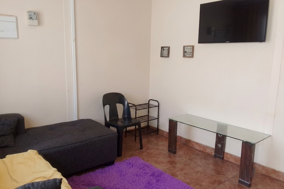 A living room area featuring tiled flooring and a wall-mounted television, providing a functional space for relaxation.