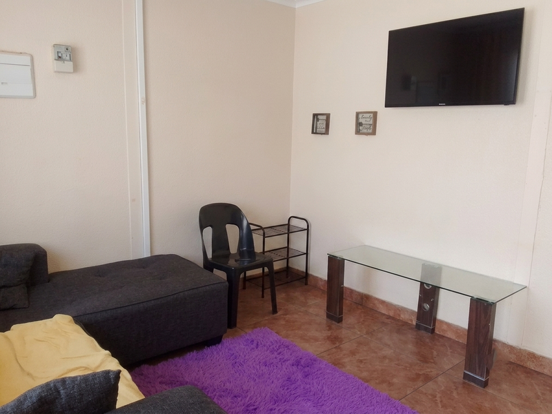 A living room area featuring tiled flooring and a wall-mounted television, providing a functional space for relaxation.