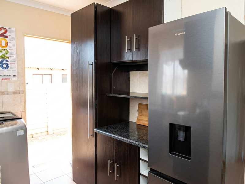 A functional scullery area featuring dark wood cabinetry, granite countertops, and tiled finishes, providing additional storage and workspace adjacent to the main kitchen.