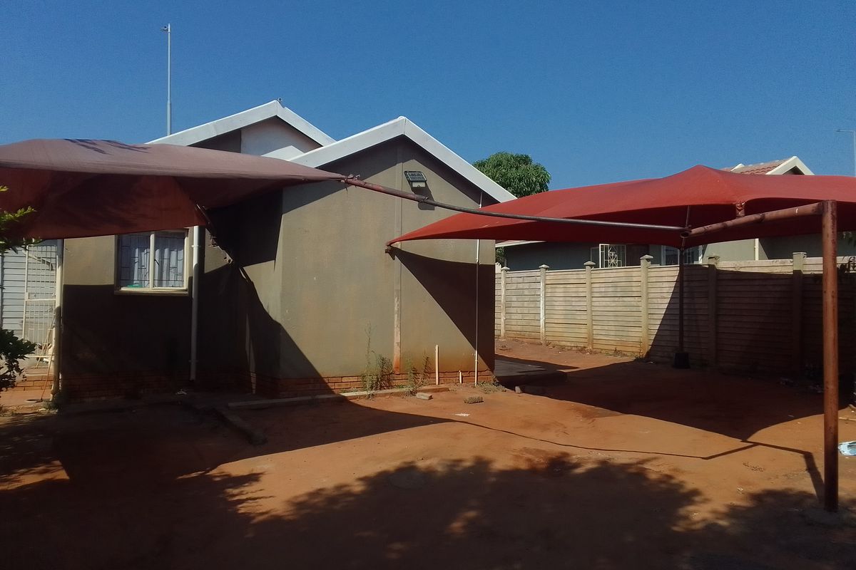 Rear exterior view of the property featuring shade sails, a precast concrete boundary wall, and an unpaved yard area.