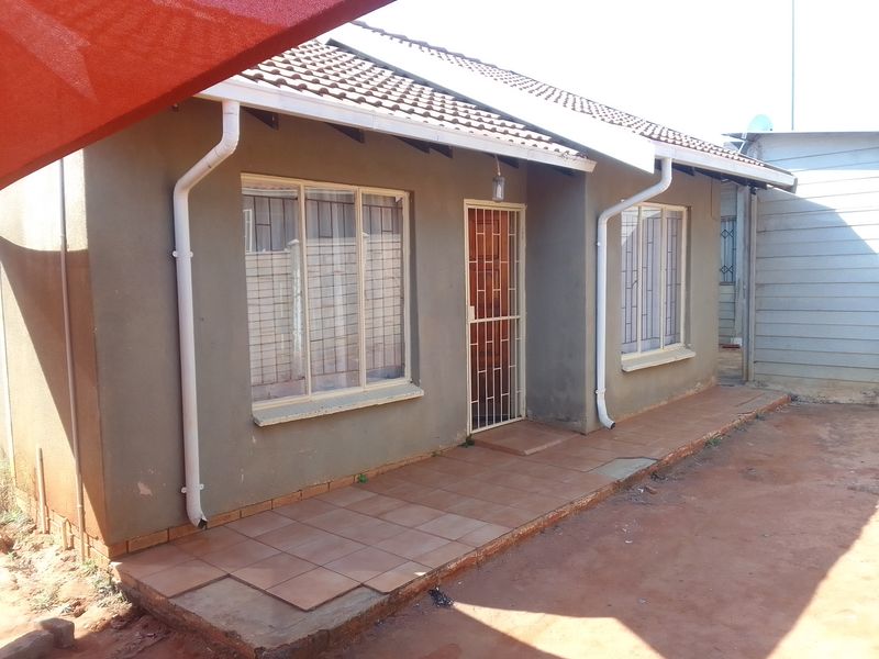 Rear exterior view of the house featuring a tiled patio area, security gates, and guttering system.