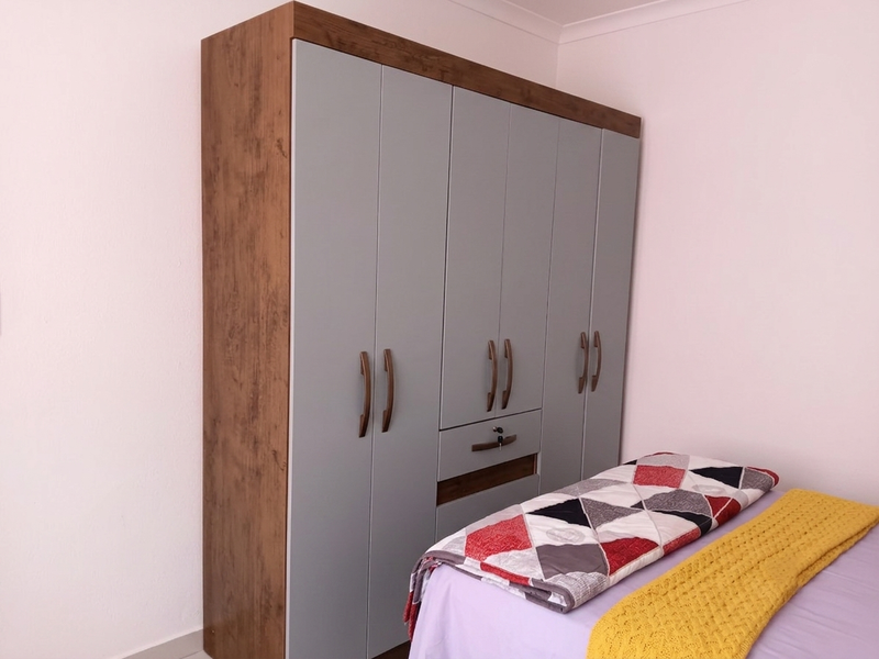 A bedroom featuring a modern, multi-door built-in wardrobe with a wood-grain frame and grey doors, providing ample storage space.