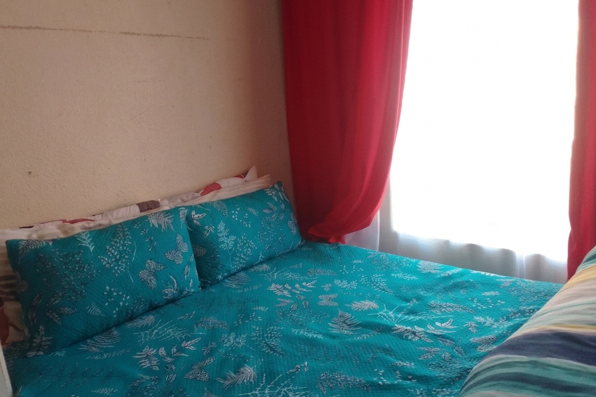 A bedroom featuring a window with red curtains and visible wall surface imperfections.