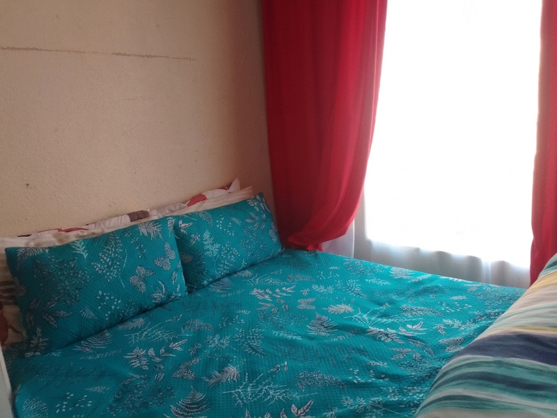 A bedroom featuring a window with red curtains and visible wall surface imperfections.