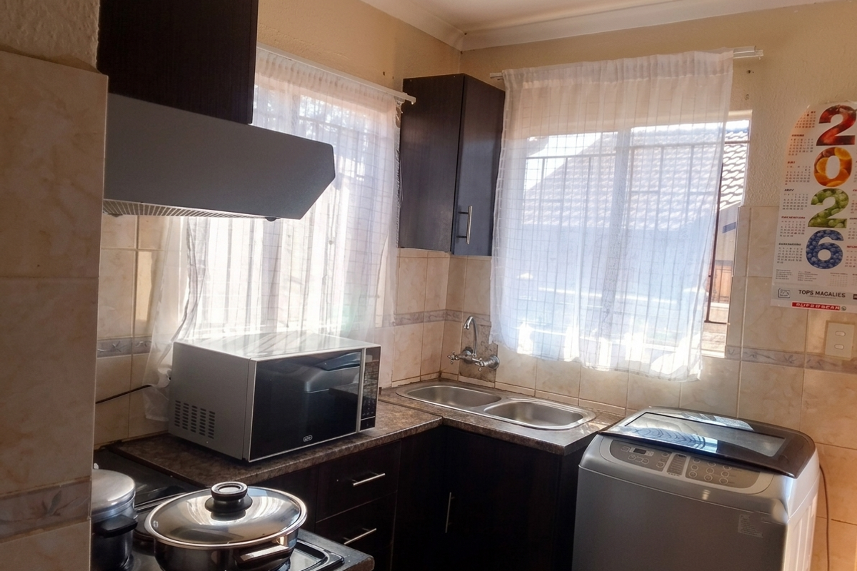 A functional kitchen featuring dark cabinetry, a double sink, tiled backsplash, and an integrated extractor fan, providing a practical workspace.