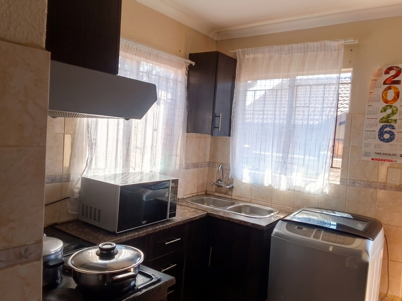 A functional kitchen featuring dark cabinetry, a double sink, tiled backsplash, and an integrated extractor fan, providing a practical workspace.