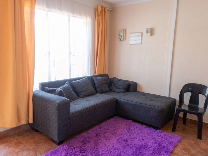 A living room area featuring tiled flooring, security bars on the window, and wall-mounted electrical infrastructure.
