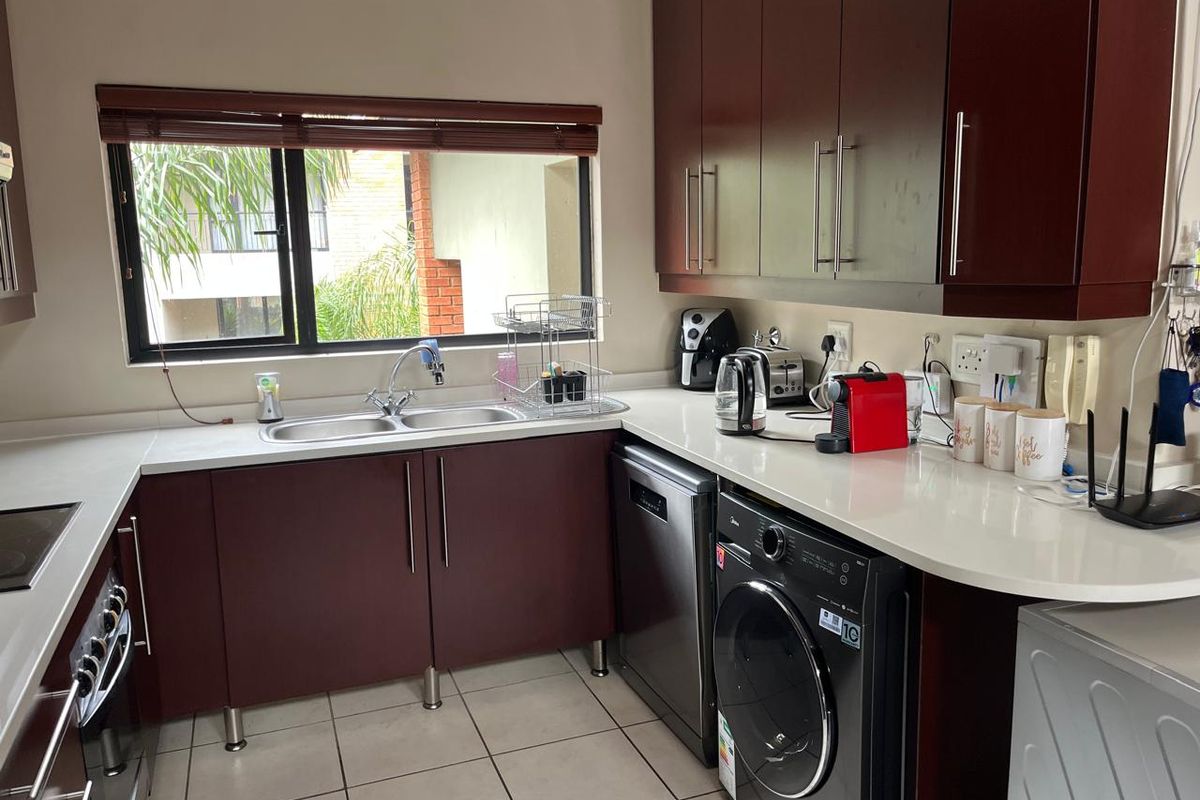 A functional kitchen featuring dark wood cabinetry, stone countertops, a double basin sink, and tiled flooring with space for integrated appliances.