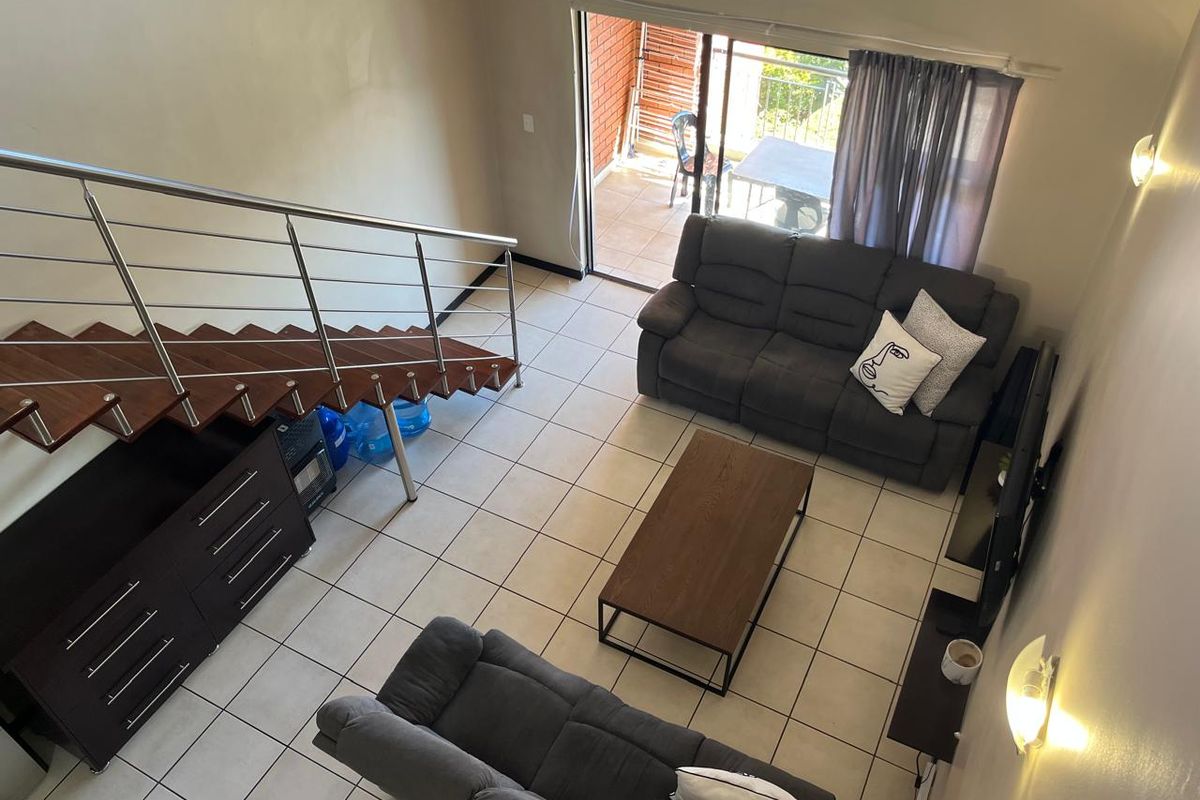 Open-plan living area featuring tiled flooring, a modern staircase with stainless steel balustrades, and direct access to an outdoor balcony through sliding glass doors.