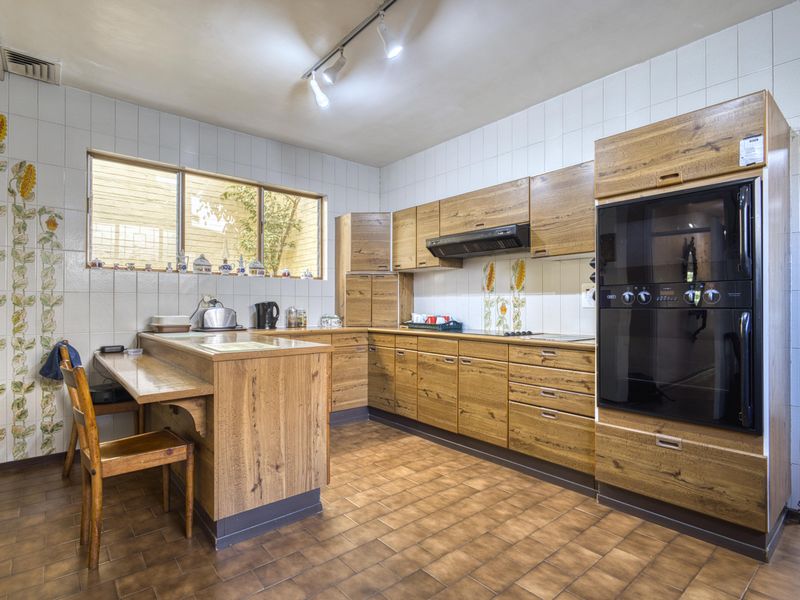 A functional kitchen featuring wood-look cabinetry, built-in oven, extractor fan, tiled backsplash, and a built-in breakfast bar with tiled flooring.
