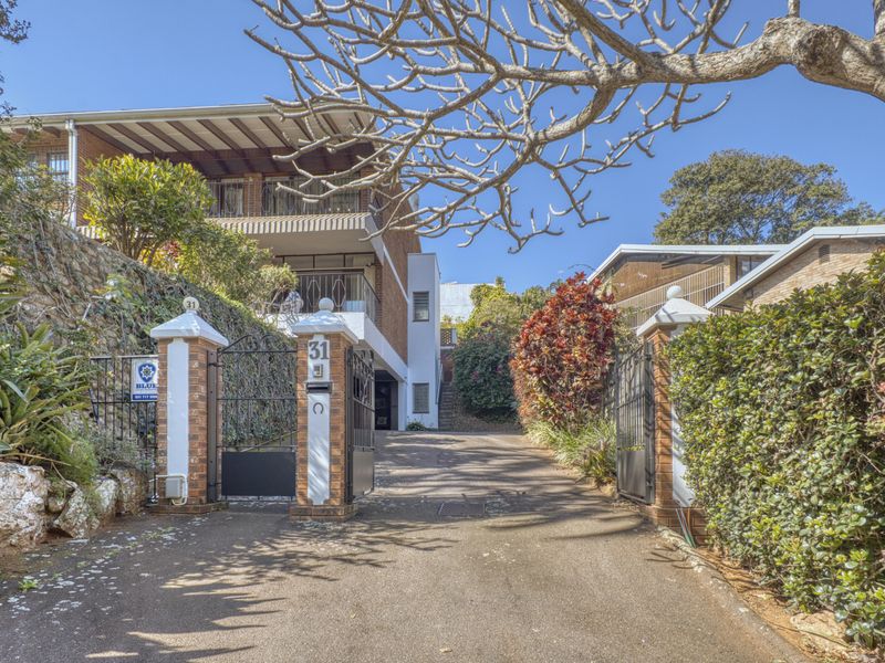 Front entrance view of the townhouse property featuring a gated driveway, brick retaining walls, and a multi-level facade with a balcony.