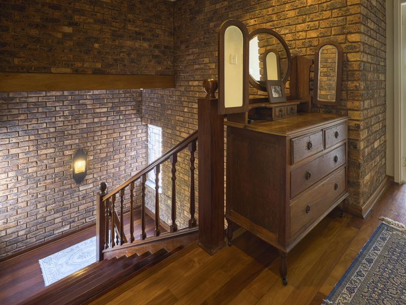 A characterful hallway featuring exposed brick walls, rich hardwood flooring, and a traditional timber staircase with a matching balustrade.