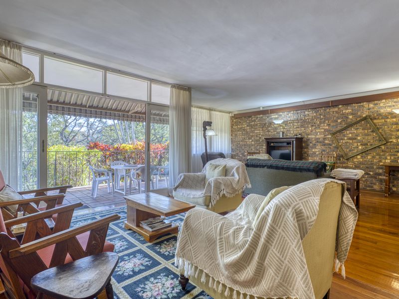 Spacious living room featuring an exposed brick feature wall, hardwood flooring, and large sliding glass doors opening onto a covered patio.