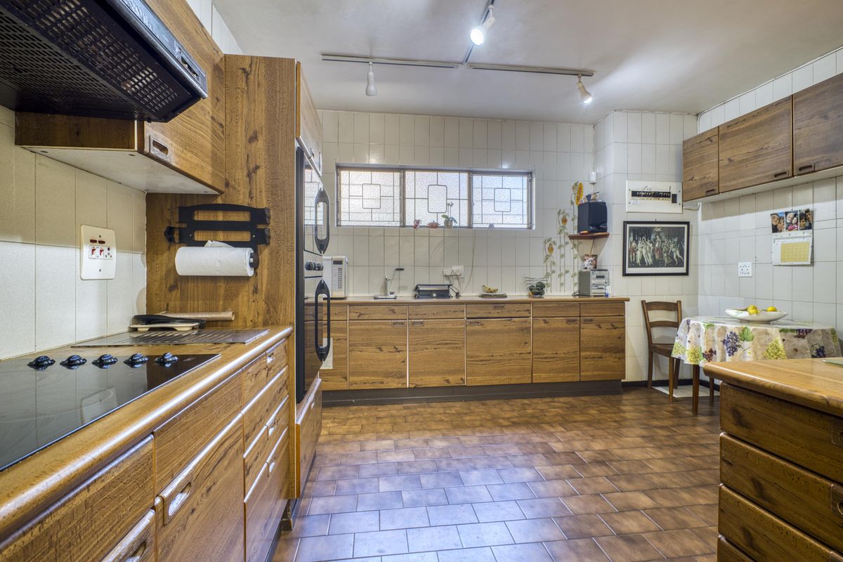 A functional kitchen featuring wood-grain cabinetry, built-in oven, electric hob, and tiled flooring, offering a classic layout with ample storage space.