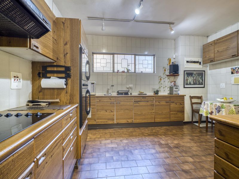 A functional kitchen featuring wood-grain cabinetry, built-in oven, electric hob, and tiled flooring, offering a classic layout with ample storage space.