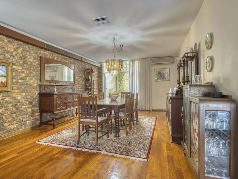 A formal dining room featuring warm hardwood flooring, an exposed brick feature wall, and direct access to an outdoor area through sliding glass doors.