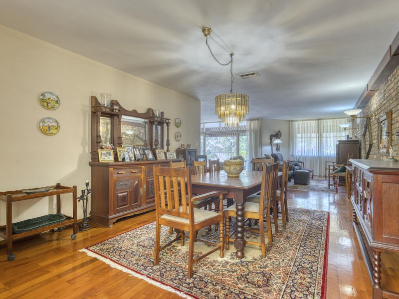 Spacious dining area featuring polished hardwood flooring, an exposed brick feature wall, and a classic chandelier, offering a warm and traditional atmosphere.