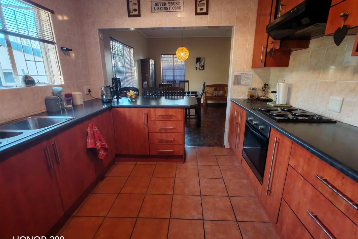 A functional kitchen featuring wood-finish cabinetry, dark countertops, built-in oven and hob, and tiled flooring, with an open-plan layout leading to the dining area.