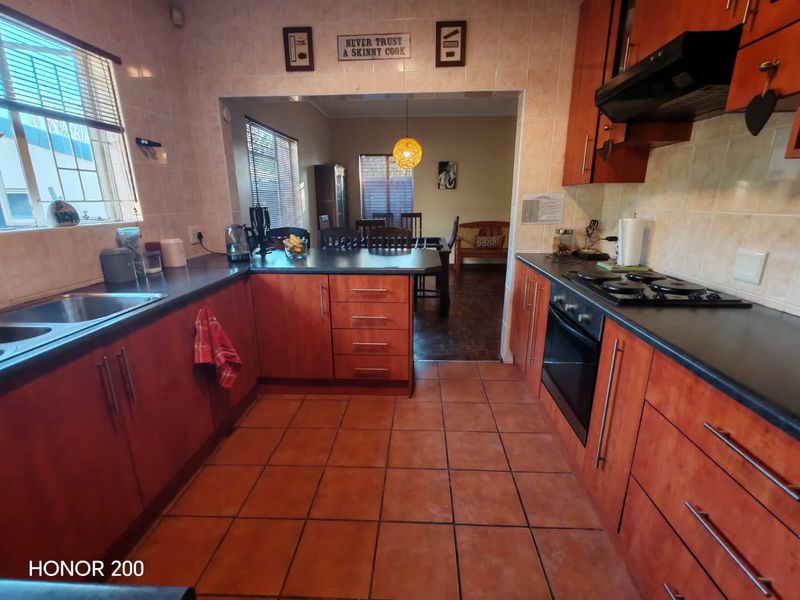 A functional kitchen featuring wood-finish cabinetry, dark countertops, built-in oven and hob, and tiled flooring, with an open-plan layout leading to the dining area.