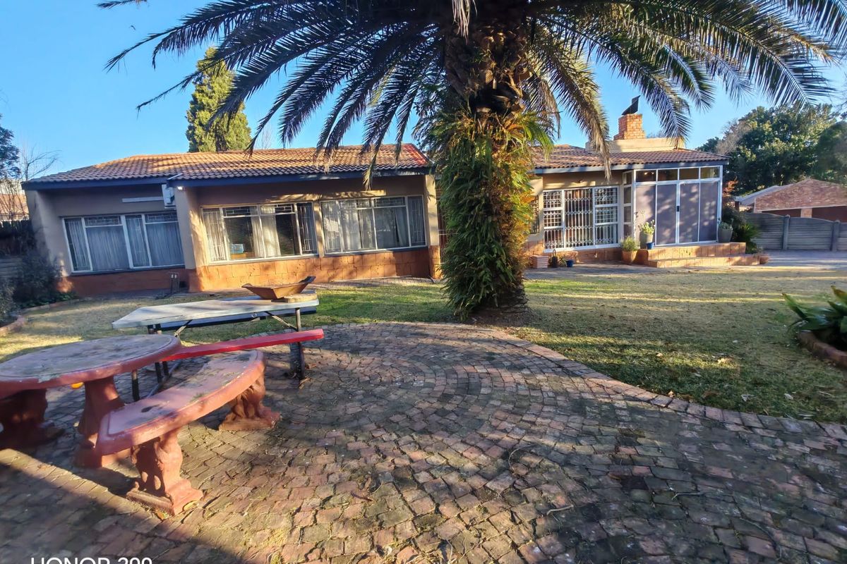 Rear view of the house featuring a brick paved patio area, established garden with a large palm tree, and traditional tiled roof architecture.