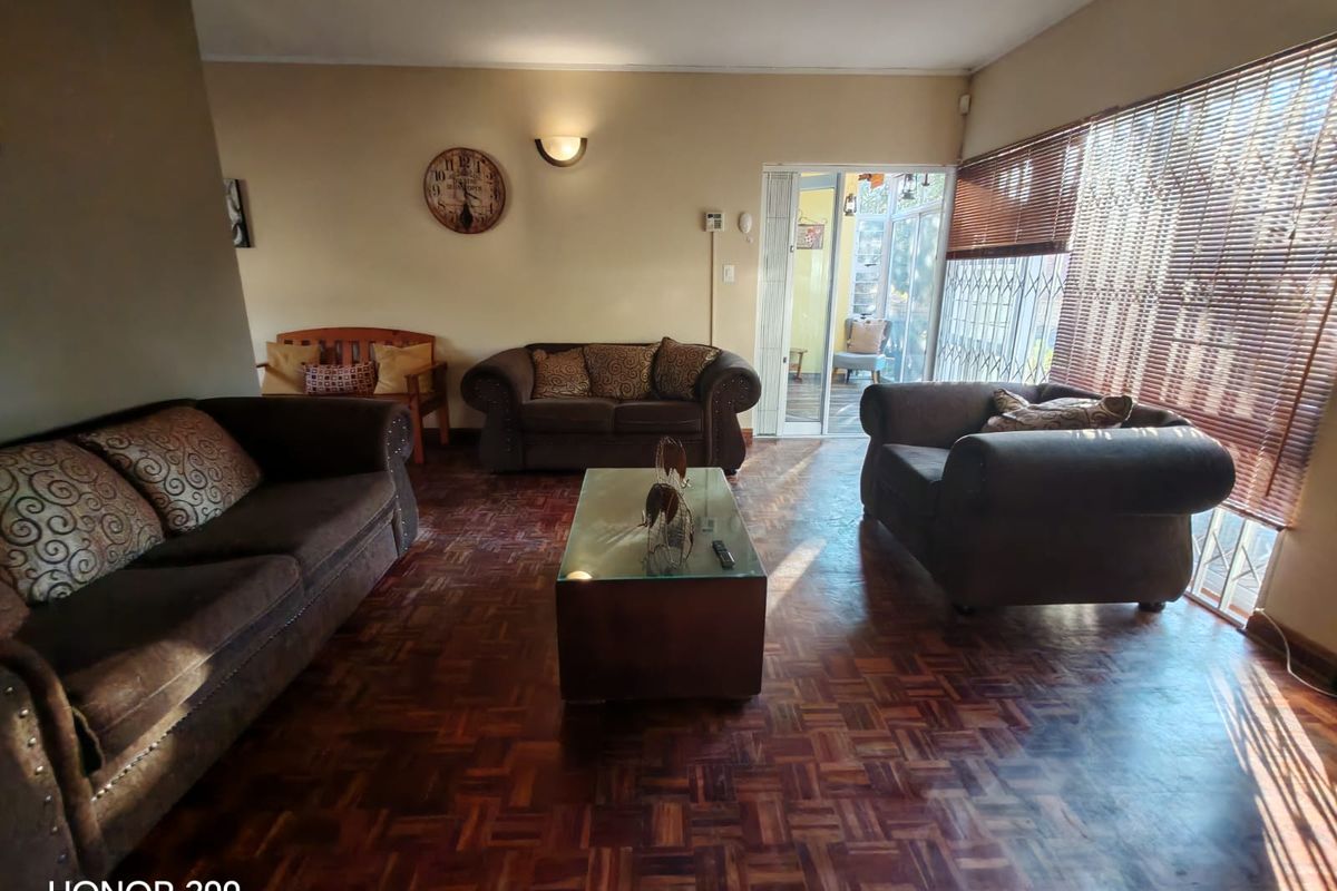 Spacious living room featuring classic parquet flooring, natural light through large windows with venetian blinds, and direct access to an outdoor patio area.